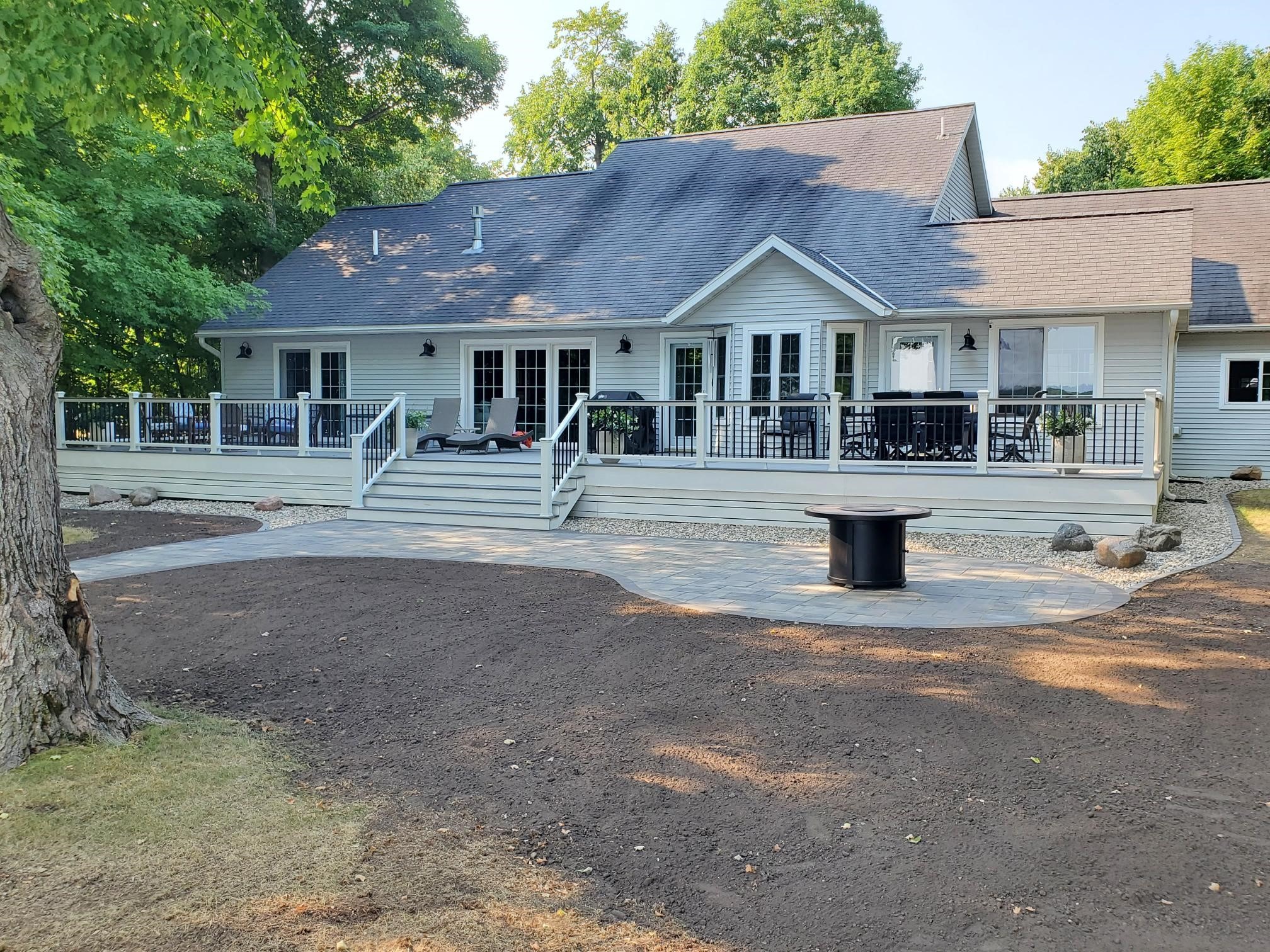 A spacious house with a large porch and surrounding greenery, featuring outdoor chairs and a table on a newly paved area.